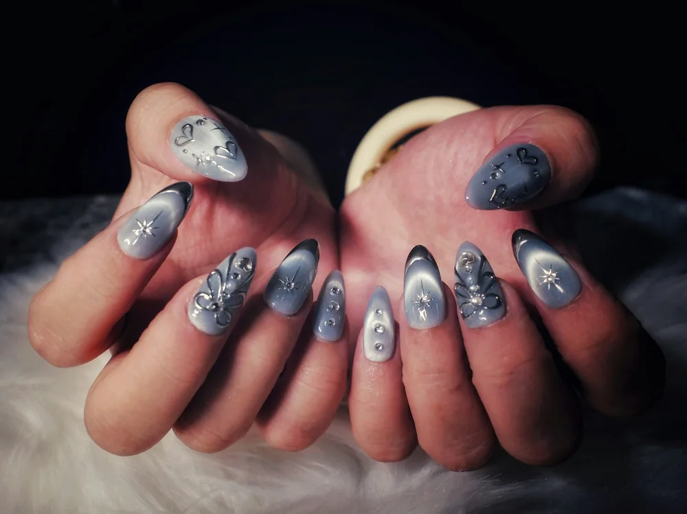 Manos con uñas almendradas en gris cat eye con brillo magnético y detalles plateados