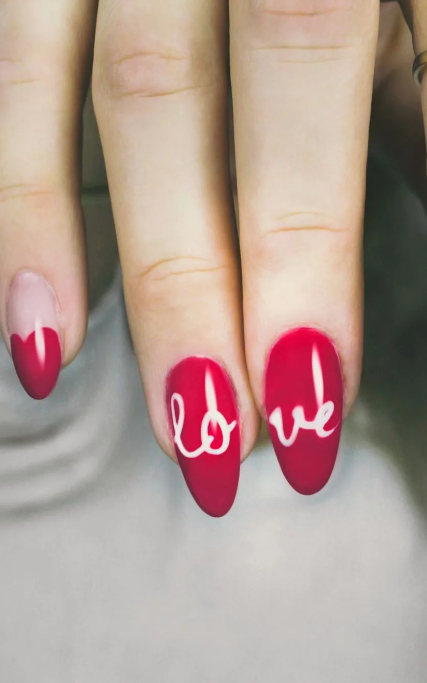 Mano con uñas almendradas rojas y rosas, una con la palabra «love» pintada